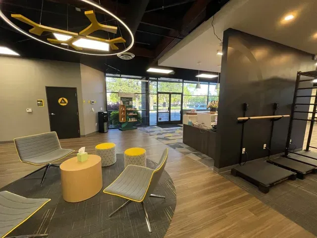 Interior of an OsteoStrong center with modern chairs, wooden table, and large circular light fixture